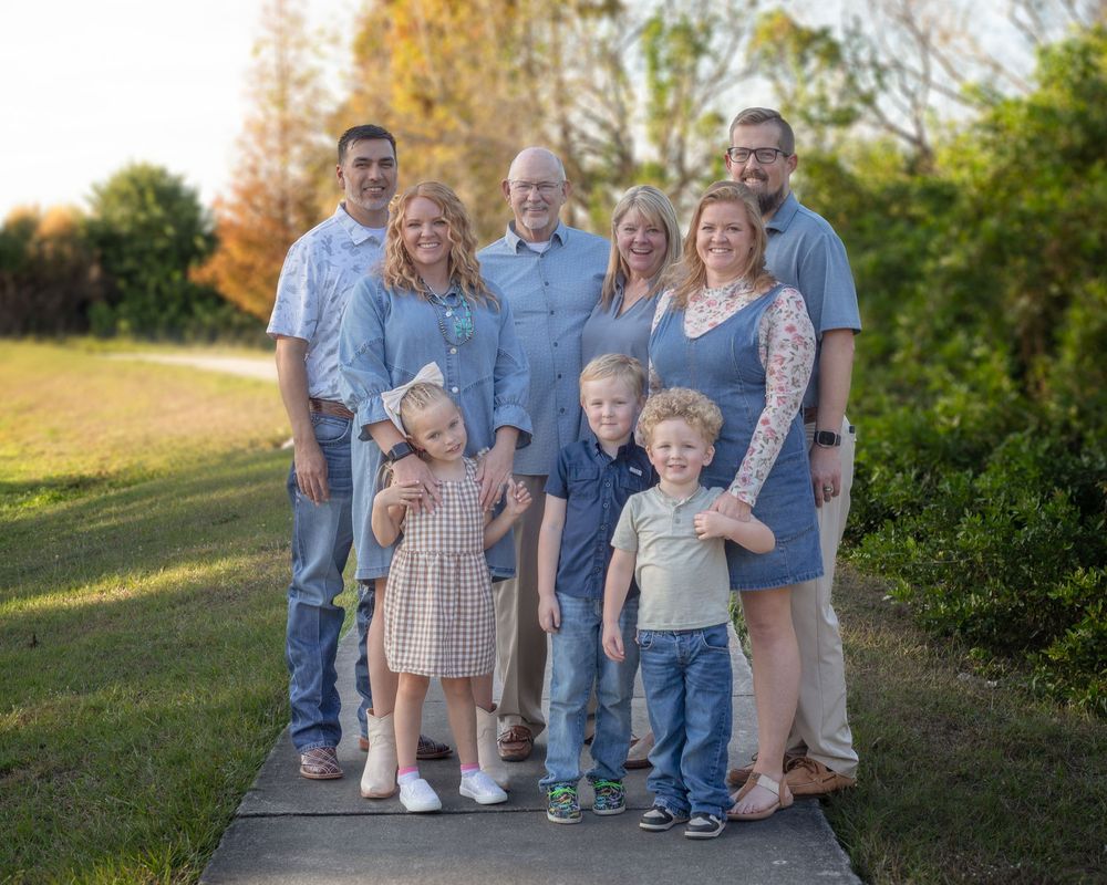 Extended family group wearing coordinated blue and neutral outfits poses together outdoors on a pathway.