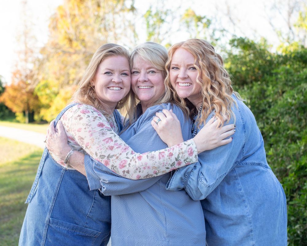 Three people embracing outdoors during golden hour with autumn trees in the background.