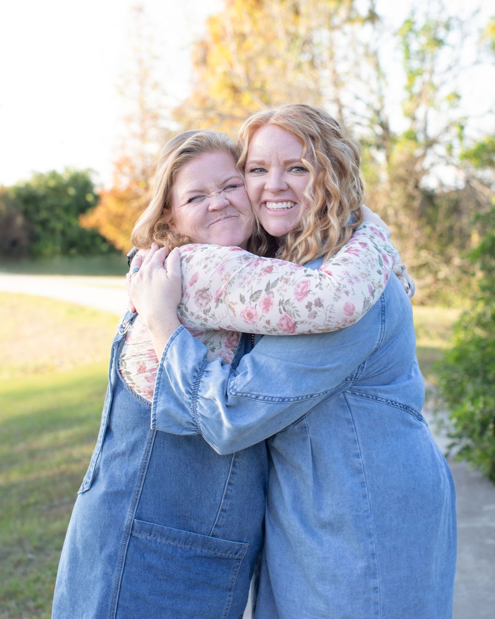 Two people share a warm embrace outdoors on a sunny autumn day wearing denim and floral prints.