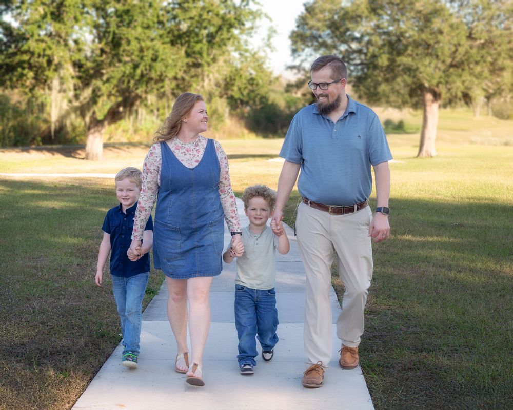 Family walking together on a concrete path through a grassy field during golden hour.