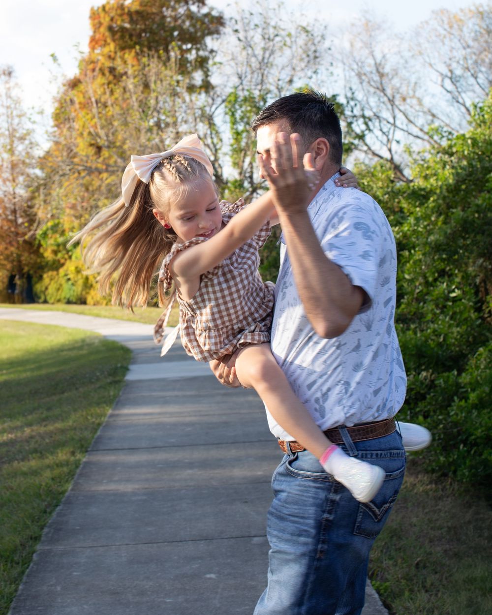 Family playfully dancing and twirling together on a paved walkway surrounded by autumn trees.