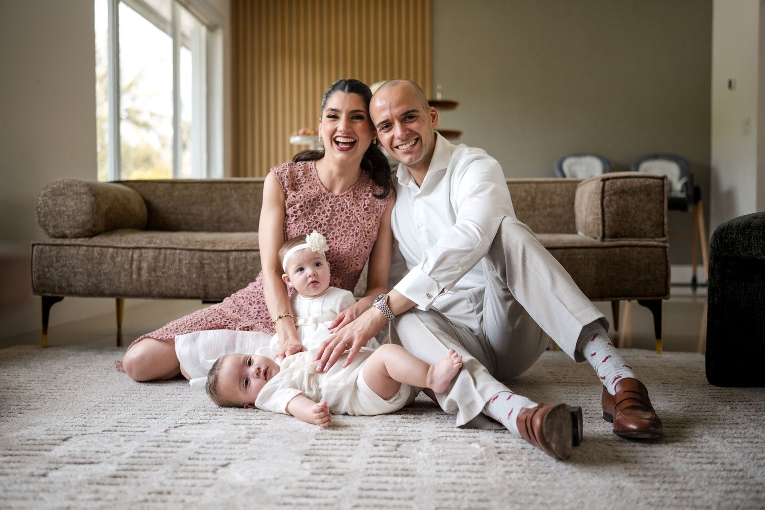 Happy family with parents and baby sitting on floor in modern living room, smiling together for portrait photo.