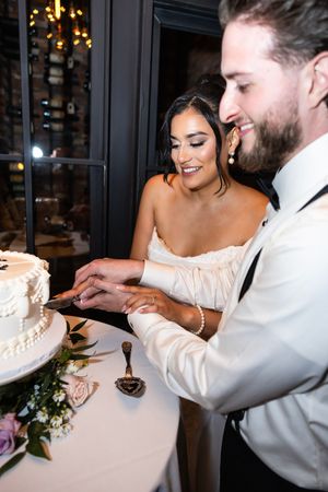 Couple sharing a playful moment during a wedding reception as they feed each other cake in a dimly lit venue. New Jersey wedding photographe