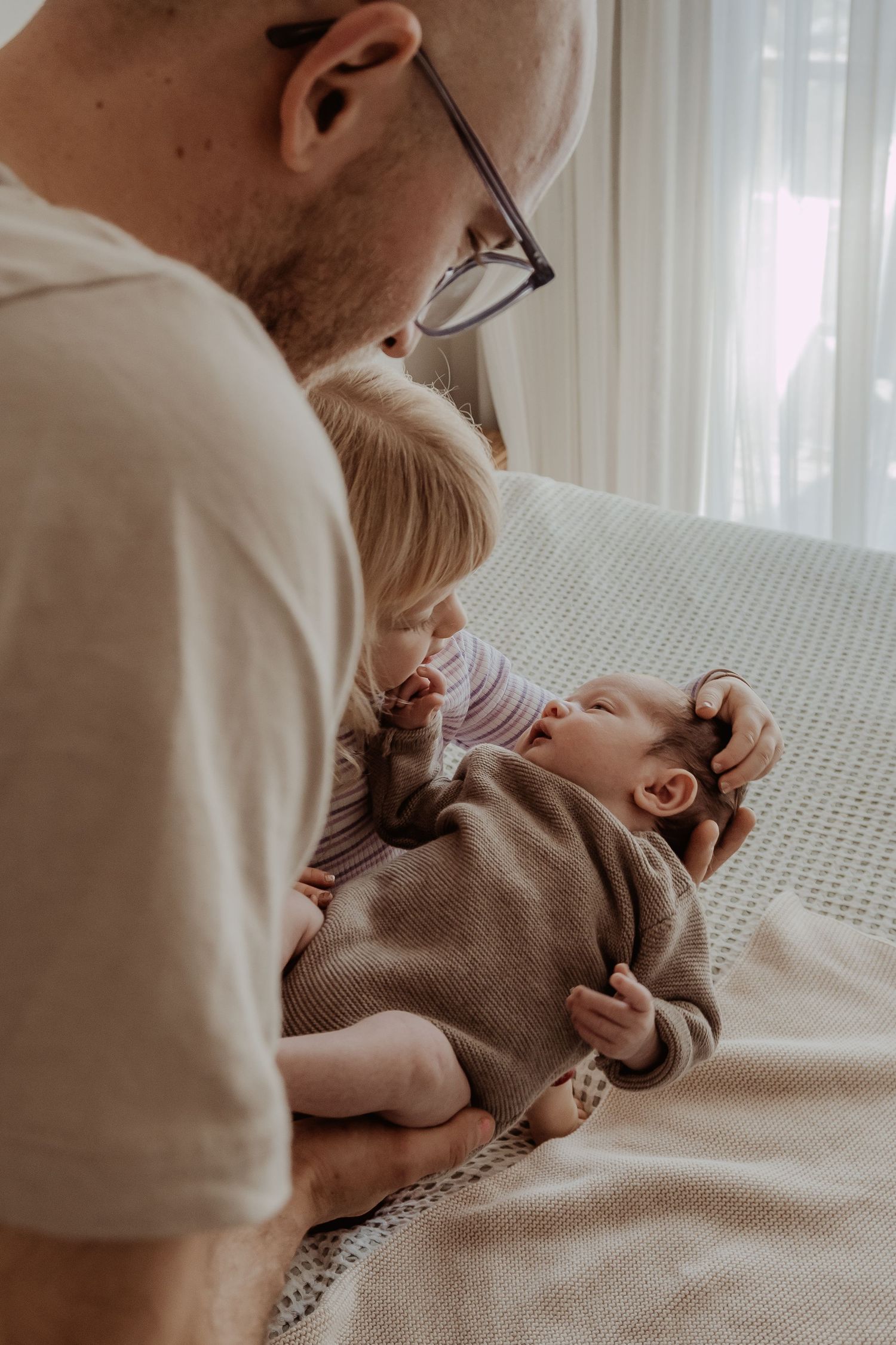Father and older sibling bonding with a newborn baby on a bed during a central coast newborn photoshoot.