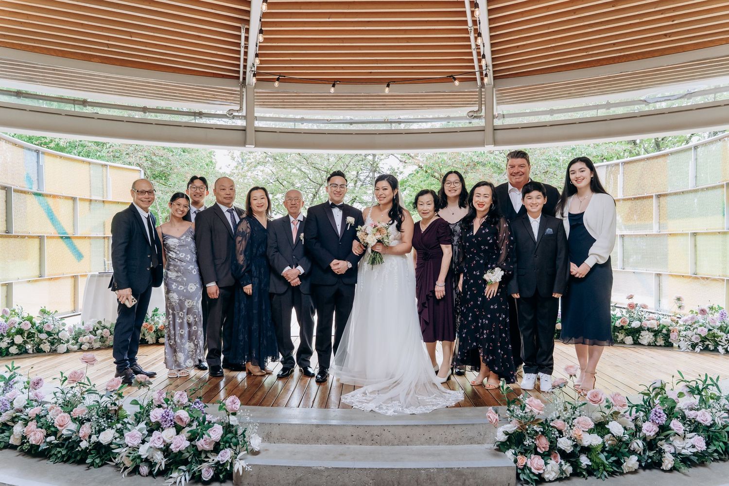 Wedding party members stand together in formal attire at an elegant venue with floral decorations and curved architecture.