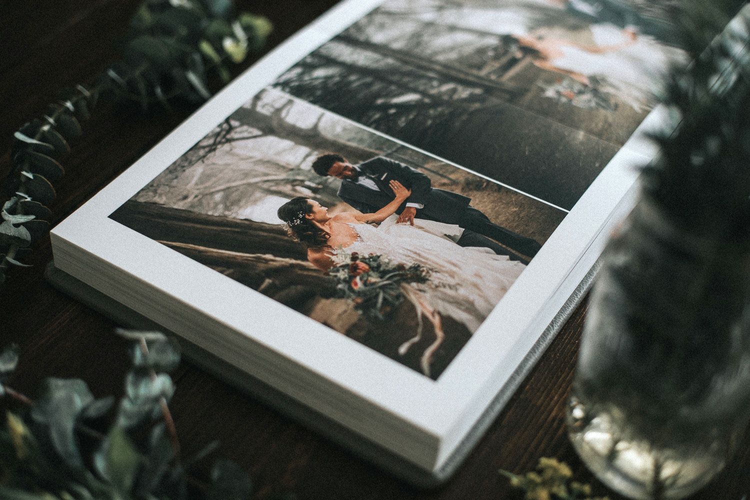Wedding photo album pages displayed with decorative foliage in dim lighting.