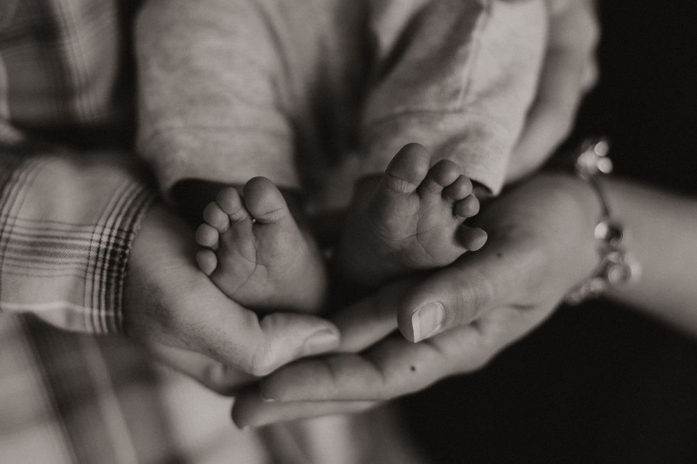 Black and white close-up photo of tiny baby feet being gently cradled in adult hands.