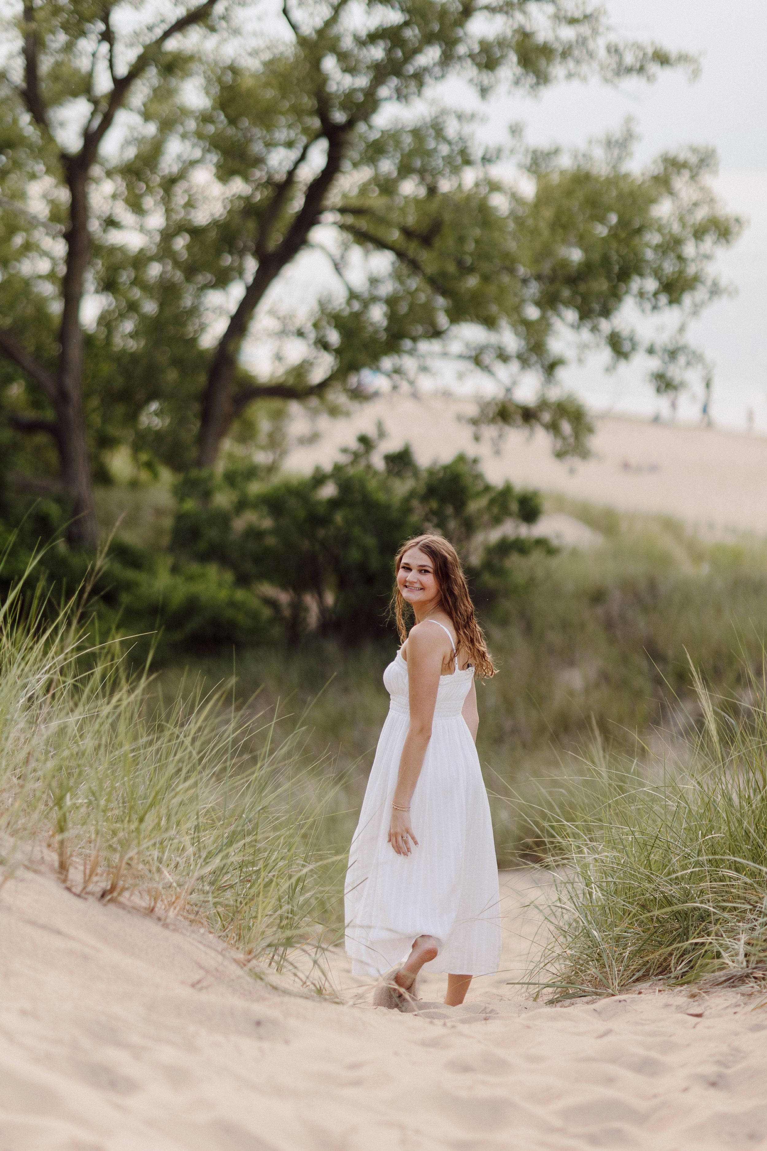 White dress flowing in the breeze as figures pose on sandy beach dunes.
