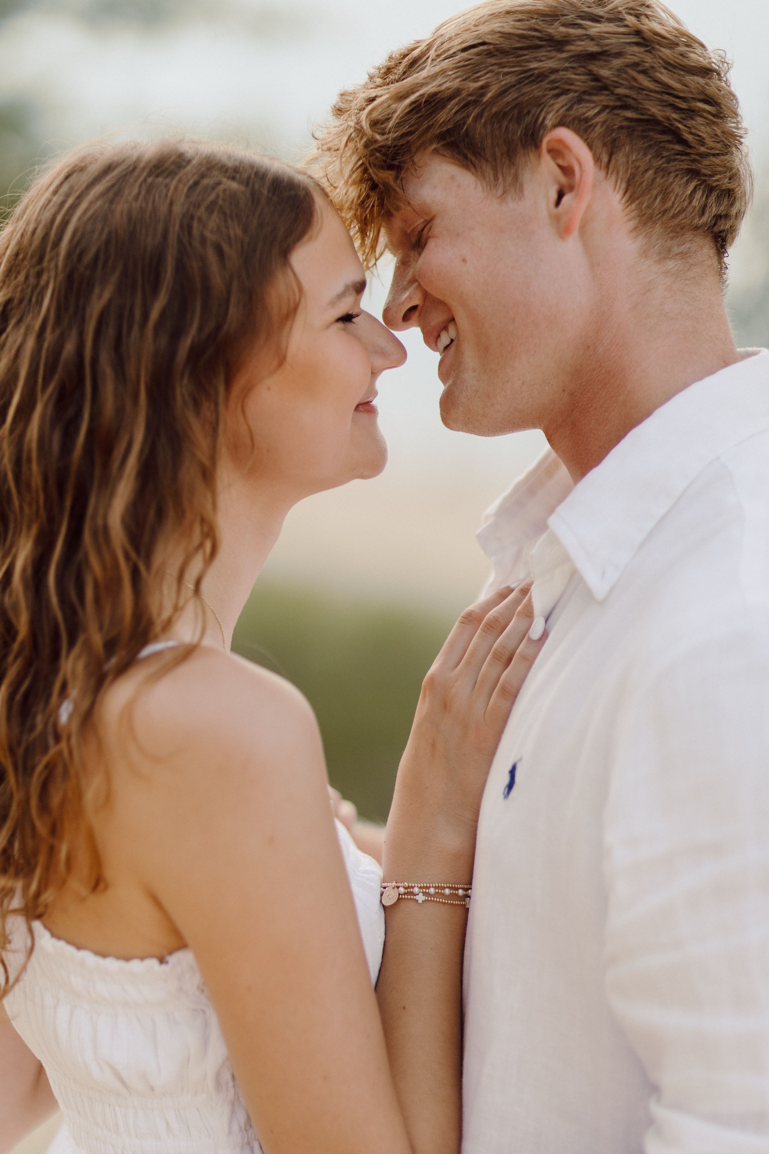 Intimate close-up portrait of couple in white outfits against natural backdrop.