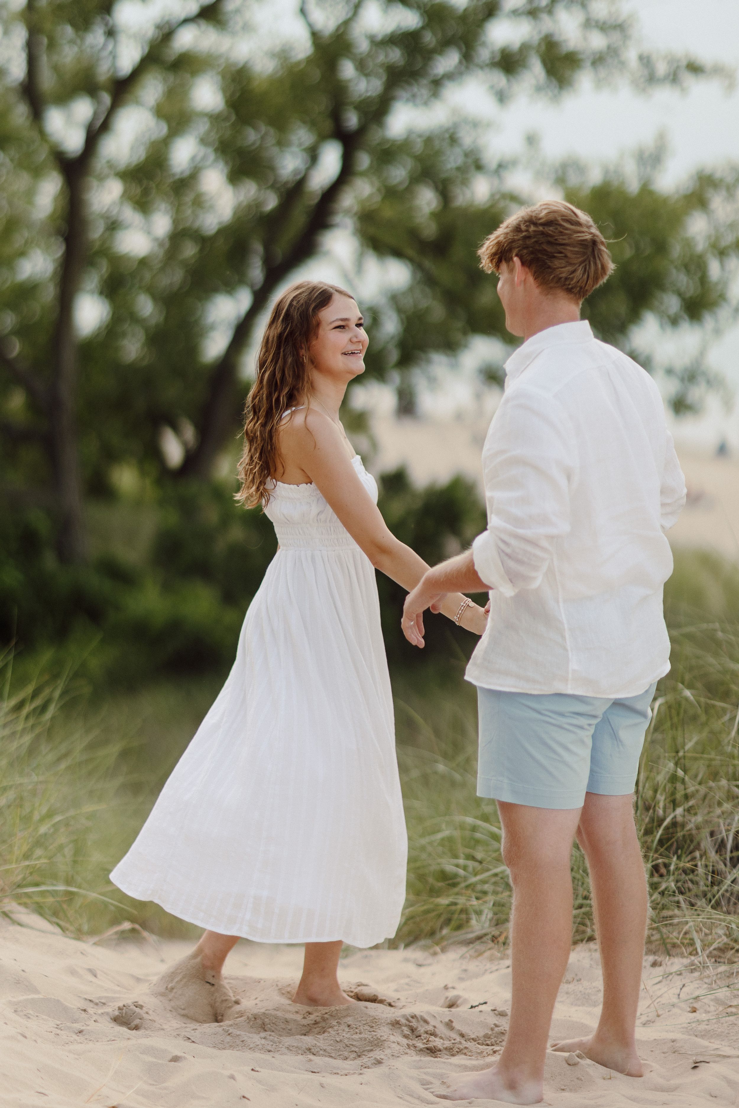 Joyful couple laughing and dancing together on sandy beach dunes.