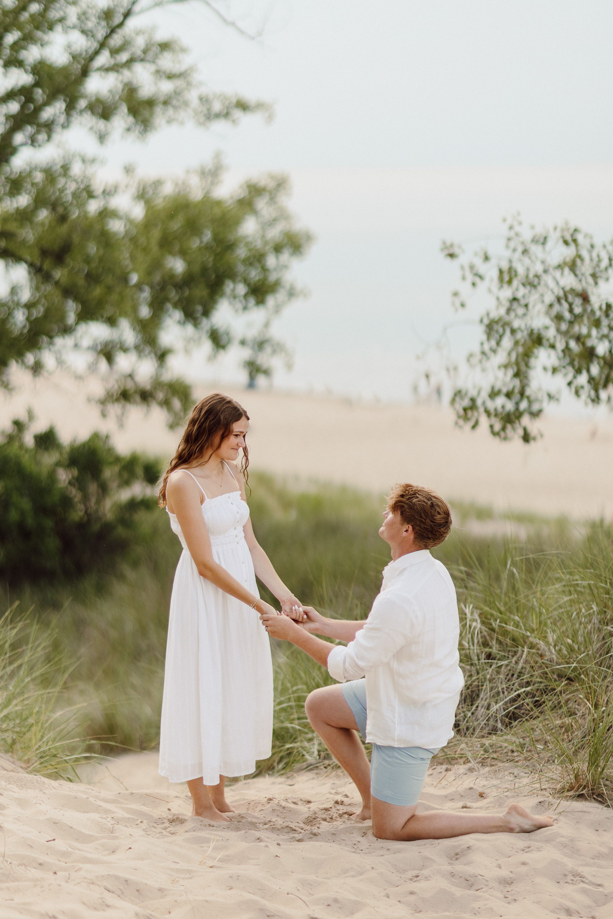 A proposal scene unfolds on a sandy beach with natural vegetation in the background.