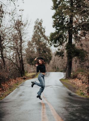A joyful dance pose on a wet forest road surrounded by autumn foliage.
