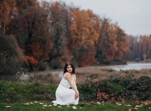 Artistic photography in an autumn setting with fall colors and a white dress by the water.
