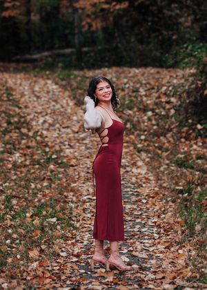 Burgundy dress and tan sweater outfit styled in a natural fall setting with scattered leaves.