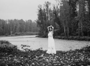 Black and white portrait by a lake showing a flowing white dress among autumn leaves.
