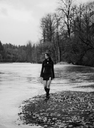 Black and white portrait of woman walking along river's edge in fall.