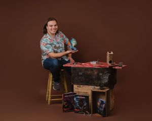 Studio portrait with fantasy props and gaming merchandise on a brown background.