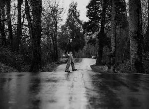 A vintage black and white photo of someone twirling on a rain-soaked forest road.