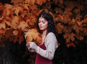 Close-up autumn portrait against dark background with golden maple leaves.