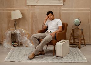 A person lounges on a beige couch reading a book in a minimalist room with warm neutral tones.