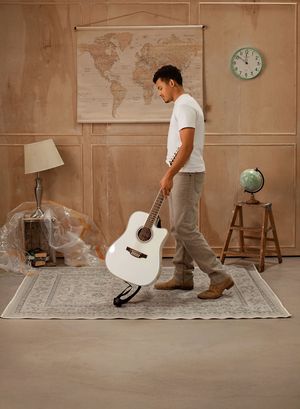 Person in cowboy boots standing on a vintage rug with an acoustic guitar against a beige wall with maps and decor.