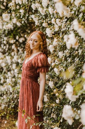 Ethereal garden scene with subject in burgundy dress amid blooming white flowers.