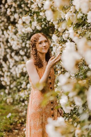 Dreamy portrait among white flowering trees in vintage-style peach dress.