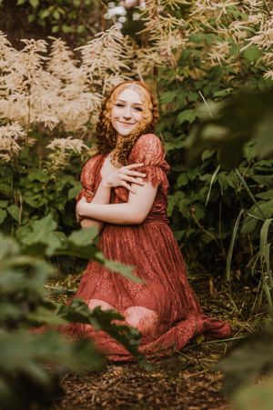 A person in a rustic red lace dress poses in a garden setting with warm lighting and greenery.