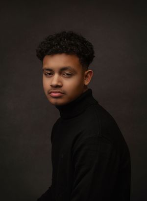 Professional studio portrait of a person in a black turtleneck against a dark background with dramatic lighting.
