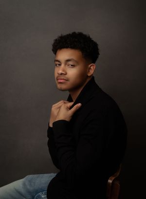 Studio portrait in black sweater against dark background with dramatic lighting.
