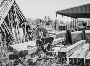 A black and white portrait on wooden planks with an A-frame structure in the background.