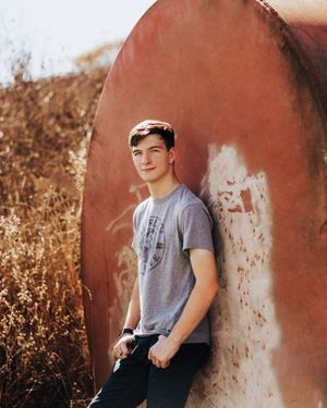 A casual portrait against a terracotta wall with tall dried grass in the background.
