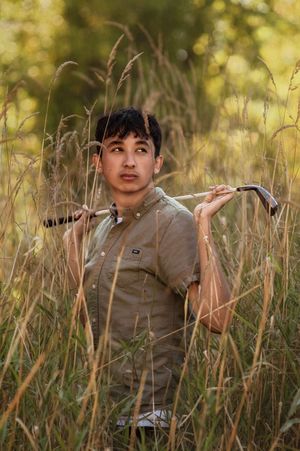 A young person sits among tall grass in a golden sunlit meadow during an outdoor portrait session.