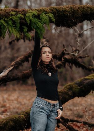 An artistic portrait under moss and ferns showing someone in a black turtleneck and jeans.