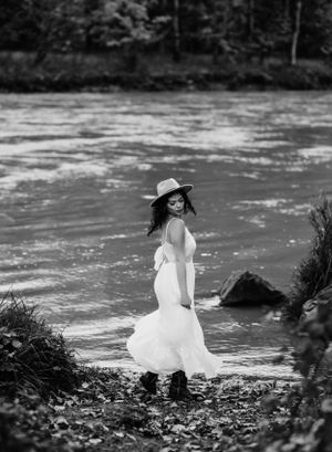 Black and white portrait by river showing flowing dress and autumn scenery.