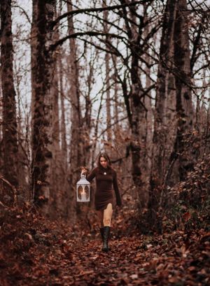 Person walks through autumn forest holding vintage lantern.