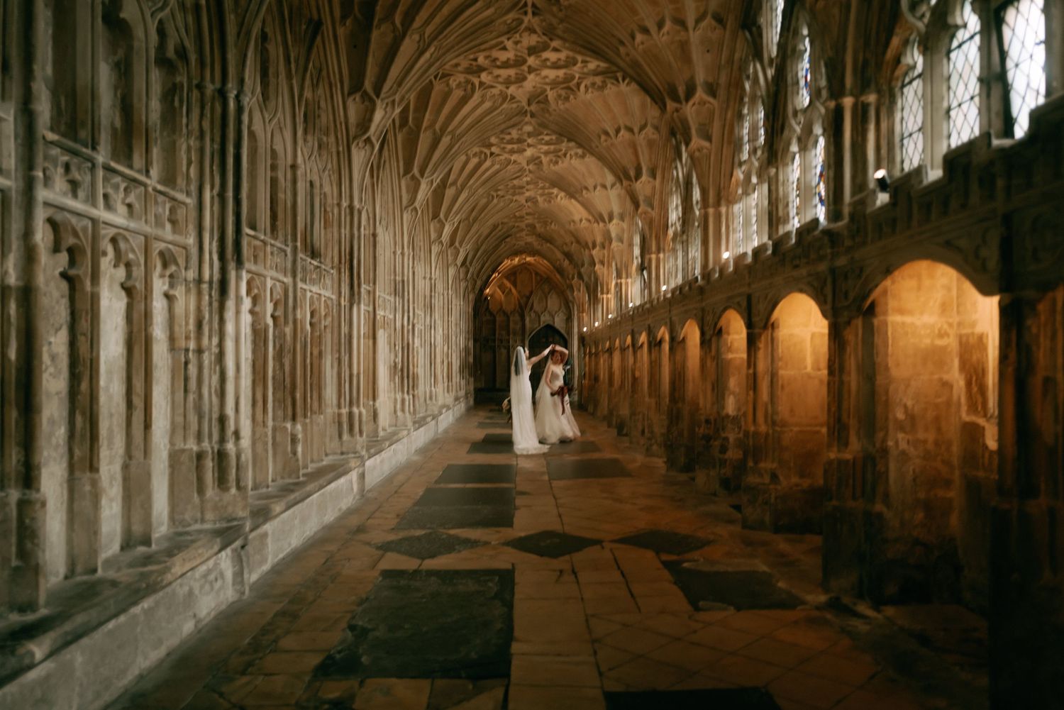 Gothic stone cloister corridor with vaulted ceiling and arched windows illuminated by dramatic natural light.