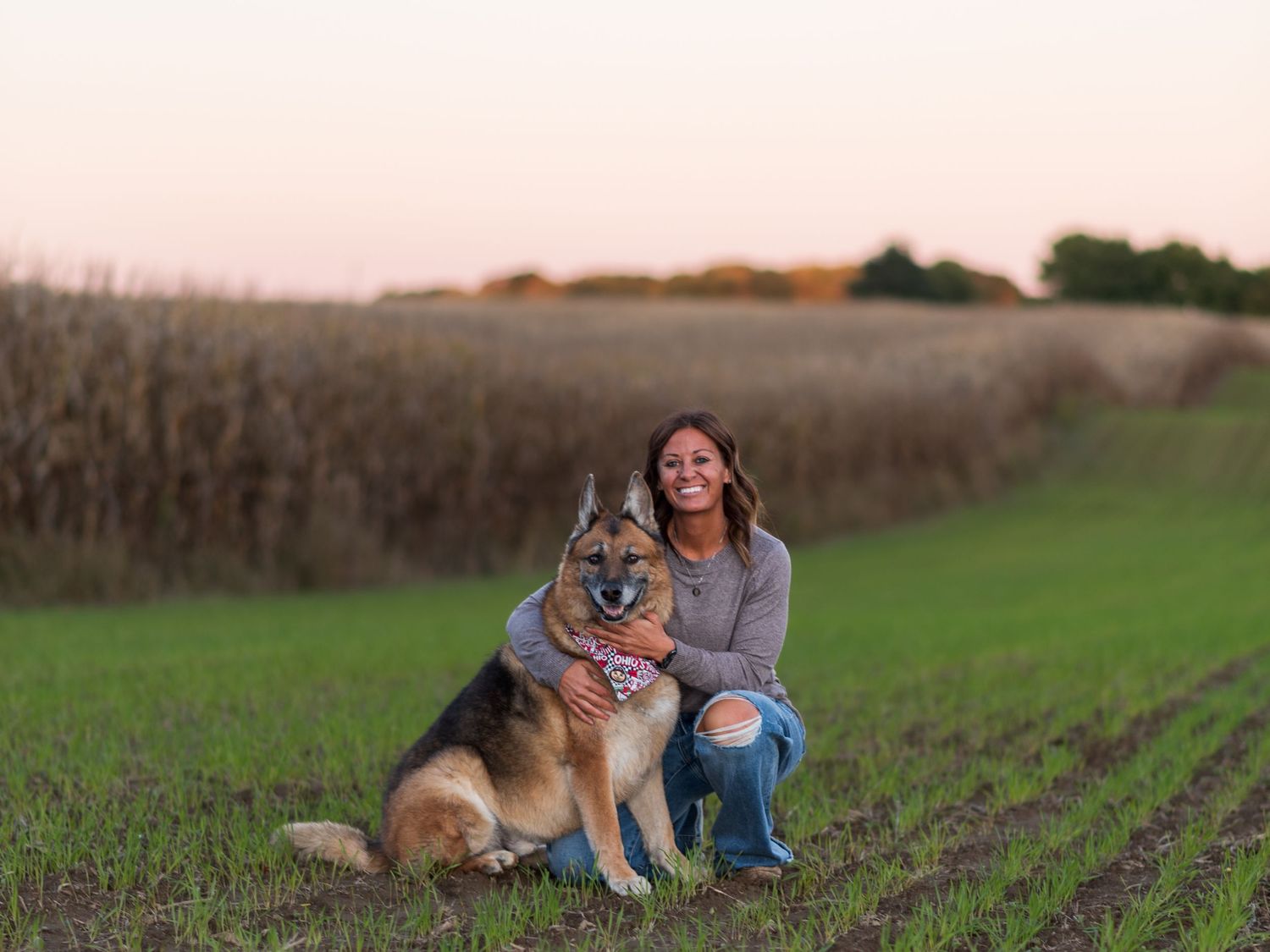 Person and dog sitting together in a grassy field at sunset.