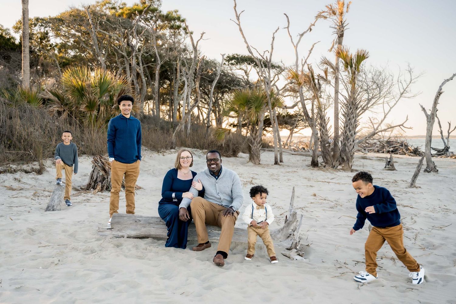 A family enjoys a tender moment together in a sunlit forest with Spanish moss hanging from trees.