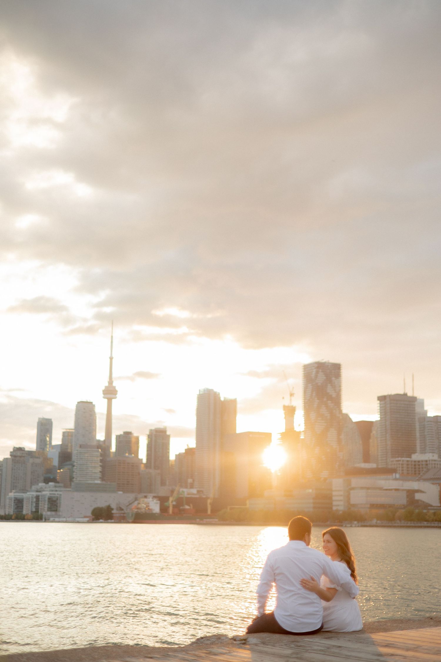 Romantic sunset silhouette of a couple overlooking Toronto's downtown skyline with CN Tower visible.