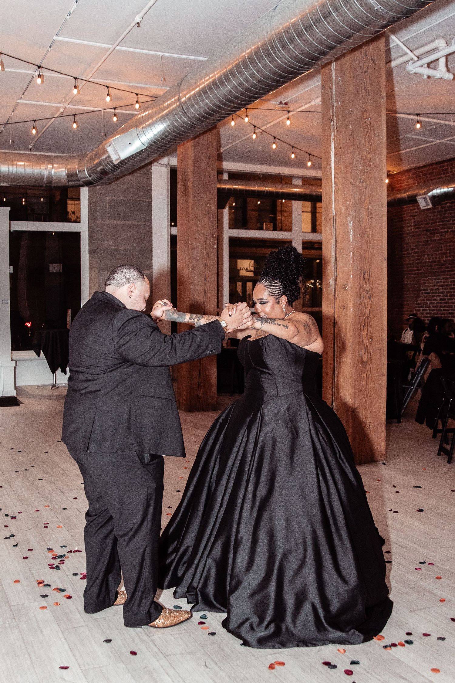 A dance between two people at an indoor venue with exposed brick walls, string lights and industrial ductwork above.