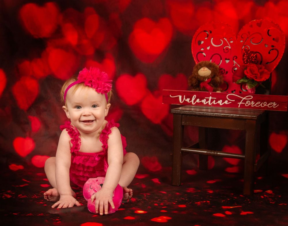Festive Valentine's Day portrait setting with red heart-shaped bokeh lights and rose petals scattered on dark floor.