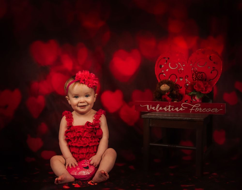 Valentine's themed portrait with red ruffled outfit and heart bokeh background featuring decorative elements.