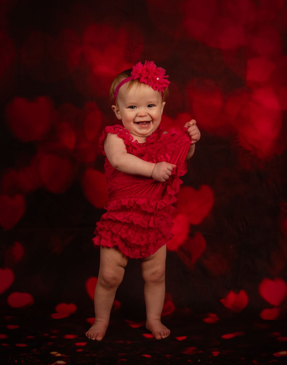 Valentine's themed baby portrait with red dress and romantic bokeh background effect.