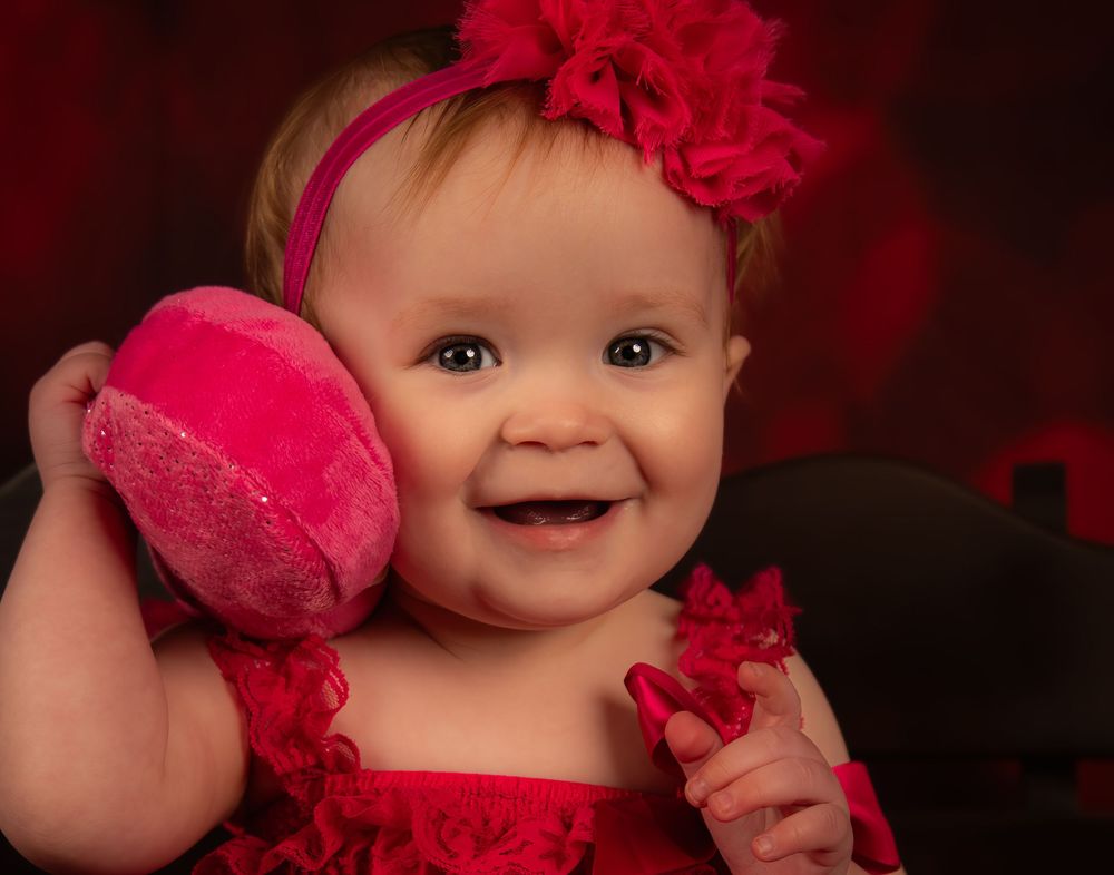 A baby wearing a bright red tulle dress and matching headband poses for a series of photos against a dark background.