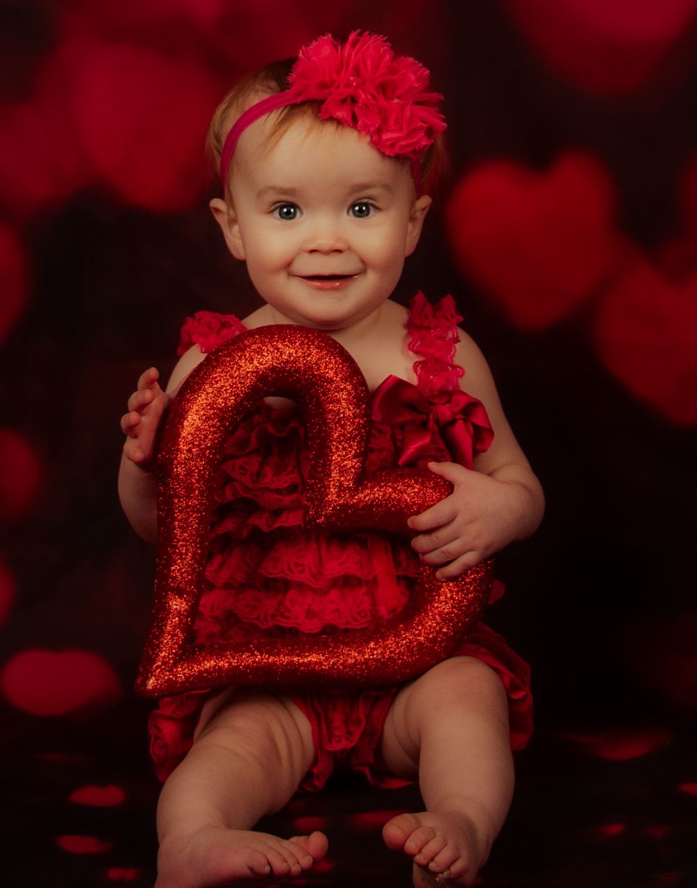 Baby in red sparkly Valentine's Day outfit and headband poses on dark background in collage of four photos.