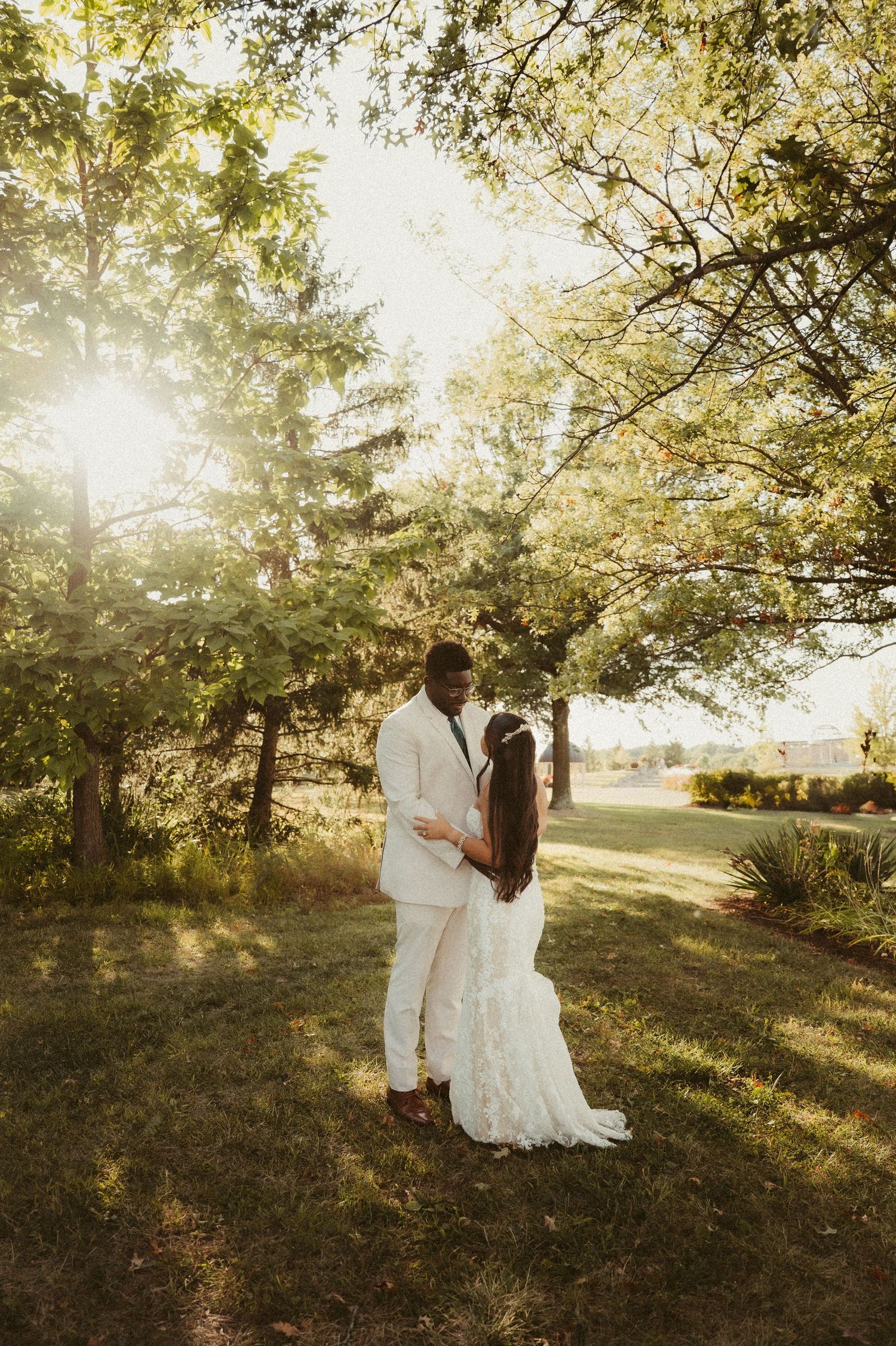 Indiana Wedding and Elopement Photographer // Couple in white attire embraces during golden hour beneath sunlit trees.