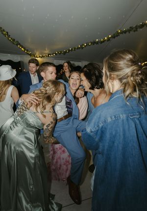 Wedding guests dancing together at a dimly lit reception with string lights overhead.