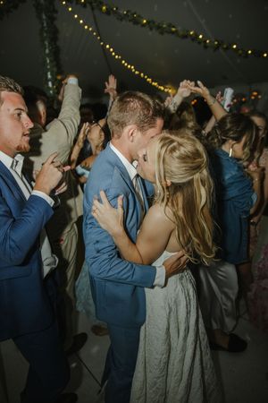 Wedding couples and guests dance joyfully under twinkling lights at an evening reception party.