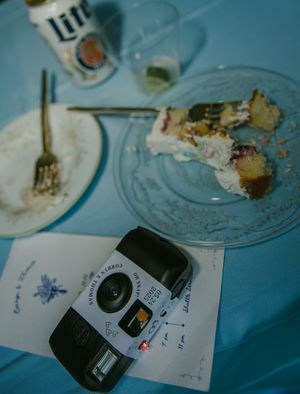 Scattered wedding dessert plates and a camera on a blue-tinted surface after a celebration.